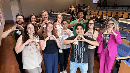 Smiling grouop of peole in auditorium, each holding hands held together to mimic Oregon O