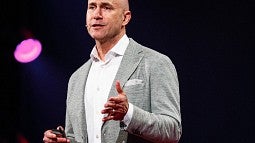 Person on stage with white shirt, gray sportjacked and tan pants with black backdrop and pink lights