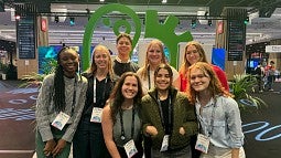 Knight Campus-based iGEM team standing before green iGEM logo statue in a conference hall