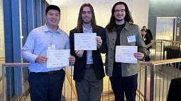 Three people standing with award certificates