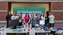 People standing in front of a banner that reads 'Bioengineering' wtih tables that have monitors and handouts