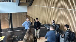 two people standing in a wooden stairwell, with cameras and microphones pointed to them, surrounded by journalists