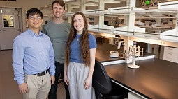 Three people standing in front of lab space, with equipment behind them
