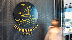 Sign with duck illustration and words reading Riverfront Bistro with blurred human figure