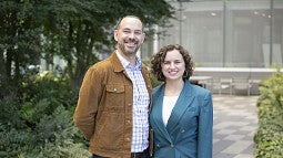 two people, a man and woman, standing next to eachother and smiling, wearing professional clothes