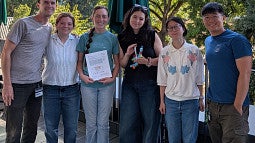 Six people standing on terrace with greenery behind