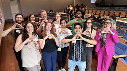 Smiling grouop of peole in auditorium, each holding hands held together to mimic Oregon O