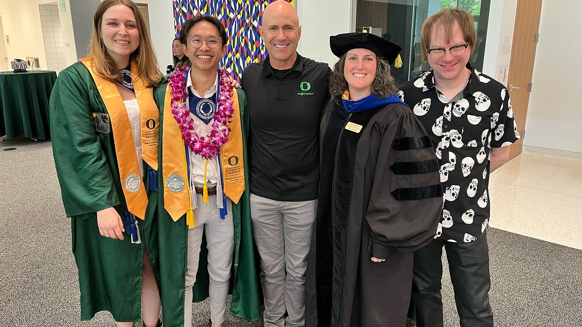 Two graduates in green regalia posing with three professors