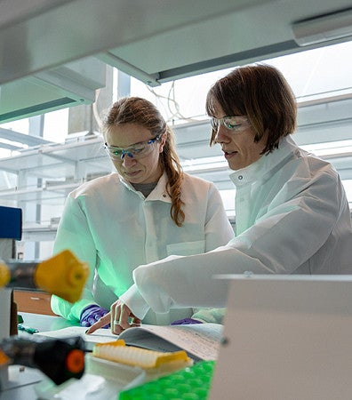 two people wearing white coats and safety goggles in a lab