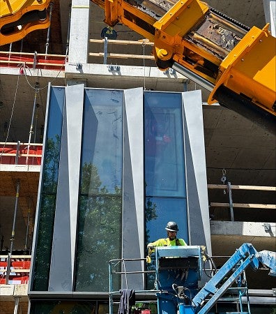 Worker in cherry picker installs glass and metal panel on outside of building