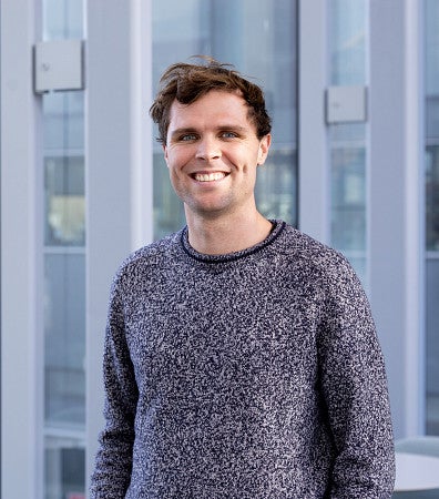 headshot of alex rockhill, in a grey sweater in front of a building