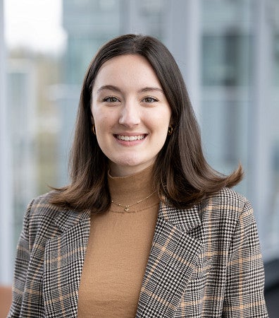 Headshot of a woman with short brown hair, in a plaid blazer, and brown top