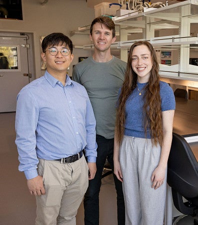 Three people standing in front of lab space, with equipment behind them