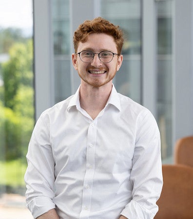 Headshot of a man with red hair, wearing glasses, and a white button-up shirt, smiling for a headshot