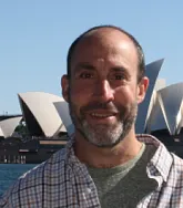 headshot of a in front of the sydney opera house in a plaid shirt