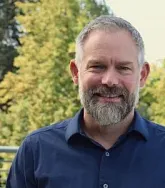Headshot of a man with a beard in front of a tree