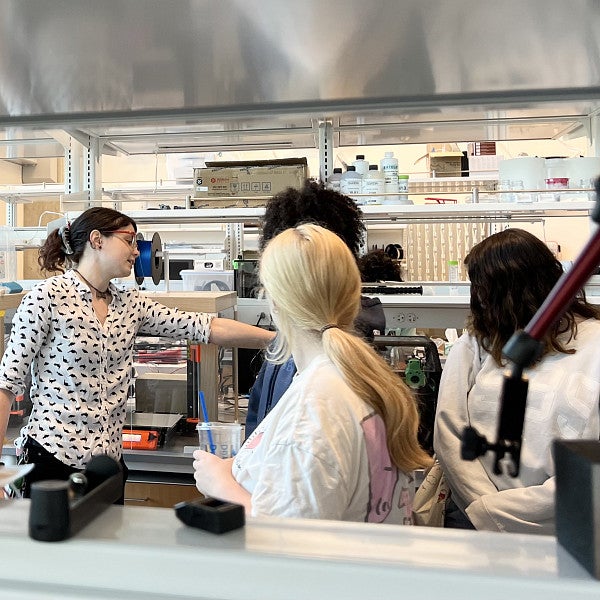 A woman points at equipment in a lab with a group of students